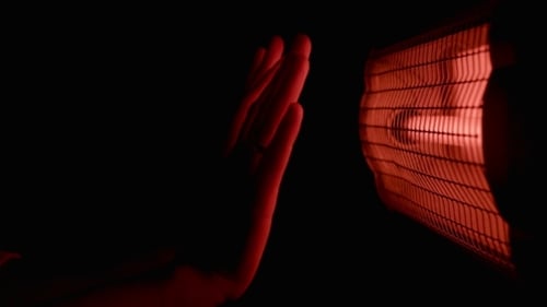 Hands Warm Up Near Red Heater at Night