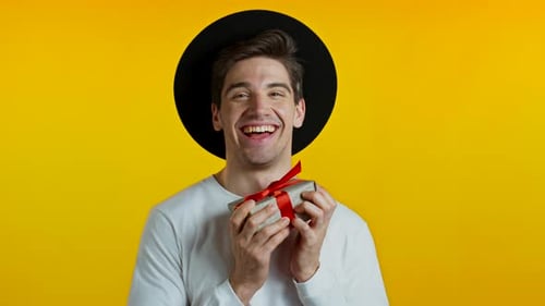 Handsome Man Holding Gift Box on Yellow Studio Background and Smiles To Camera. Happy European