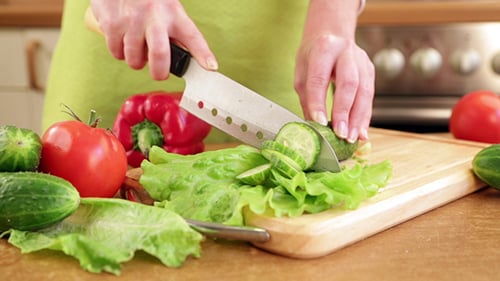 Woman Slicing Cucumber on Wooden Cutting Board