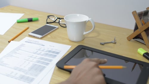 Hand Writes on Paper and Uses Tablet at Desk