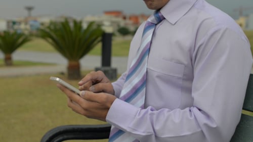 Adult Using Smartphone on Bench in Urban Park