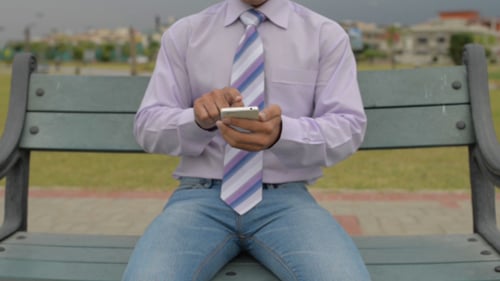 Man Using Smartphone While Sitting on Bench in Park