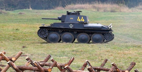 Tank Driving on Green Field Near Fence