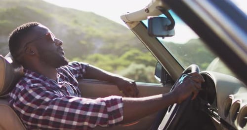 African american man with hands on steering wheel sitting in the convertible car on road