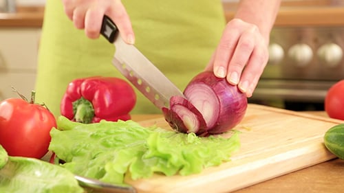 Woman Slicing Red Onion With Knife In Kitchen