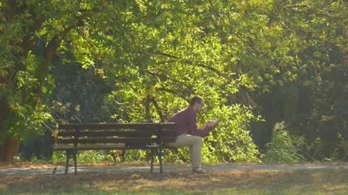 Mann sitzt auf der Bank und liest ein Buch