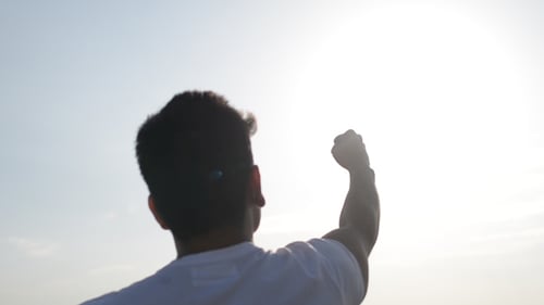 Man Silhouetted Against Sun Raises Fist in Triumph