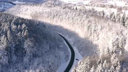 Reibungsloser Drohnenflug über eine Winterwunderlandschaft mit einer leeren Straße in einem Tal, ein wenig nach links fliegend