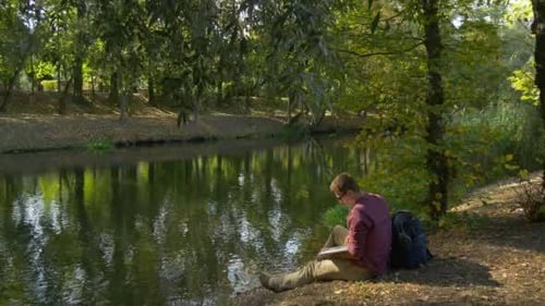 Man Working On Laptop Beside River in Park