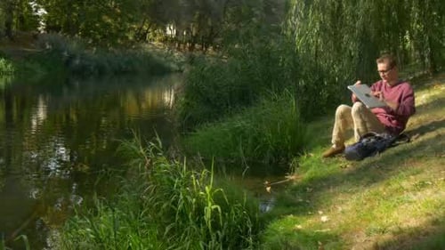 Man Using Laptop by Tranquil Waterside Park