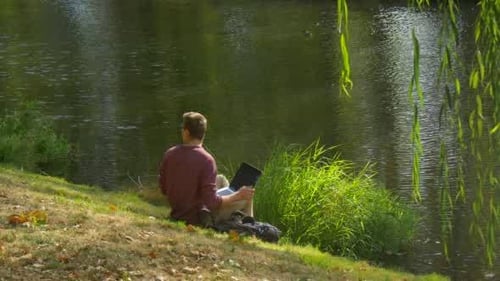 Man in Glasses is Sitting at River Bank Freelance