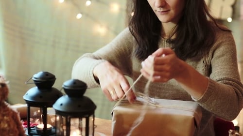 Woman Wrapping Christmas Gift with String at Table