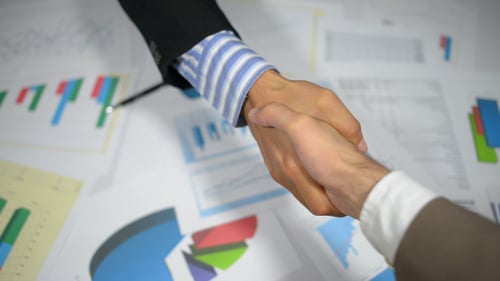 Business Handshake Over Charts and Graphs