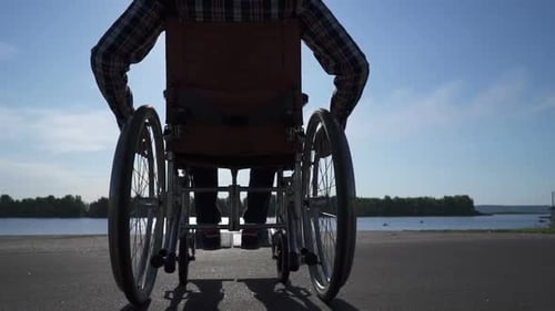 Man in Wheelchair on Paved Path by Lake