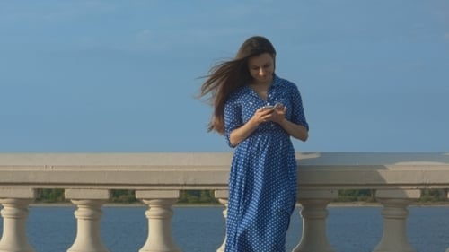 Woman Using Phone by Waterfront on a Breezy Day