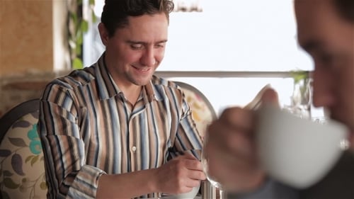 Smiling Young Man Uses Phone at Restaurant Table