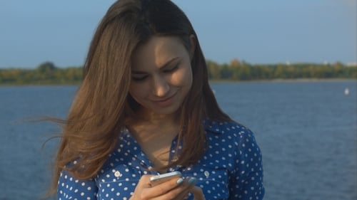 Woman Smiling at Mobile Phone by the Water