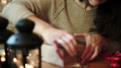 Woman Wrapping Christmas Gift with Lanterns on Table