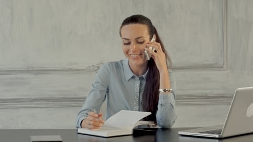 Woman Writes and Talks on Phone in Office