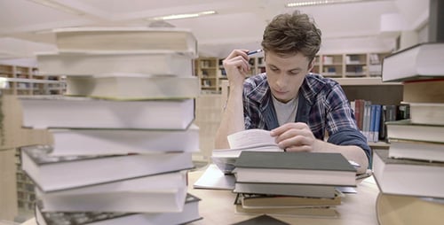Student Studying Hard Surrounded by Books in Library