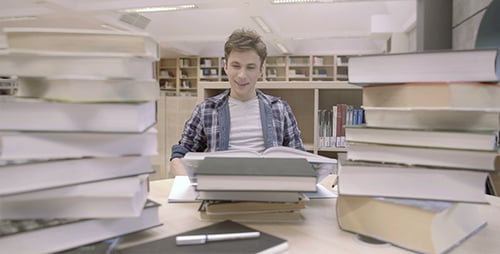 Student Studying Among Piles of Books in Library