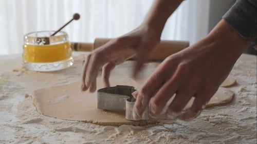 Person Cutting Cookie Shapes from Dough on Table
