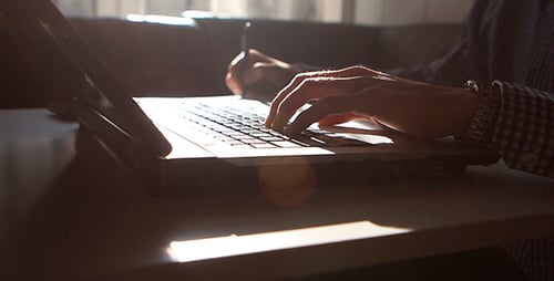 Man Working On Laptop And Writing In a Notebook