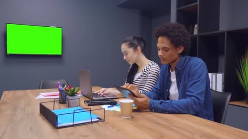 Coworkers Work Together at Desk with Green Screen TV