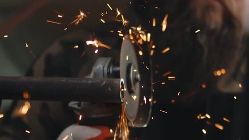 Mechaniker schneidet Metallrohre, aus denen Funken fliegen, mit Hilfe eines Winkelschleifers Nahaufnahme