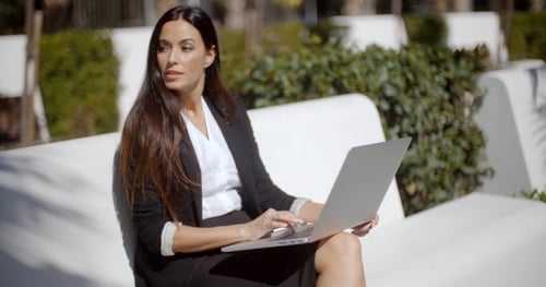 Young Woman Using a Laptop On a White Park Bench