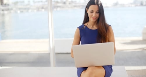 Frau sitzt auf einer Bank am Wasser mit einem Laptop