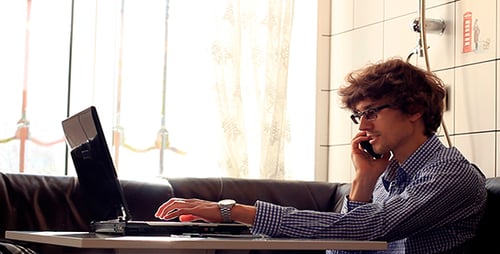 Young Man Works On Laptop and Talks On Phone