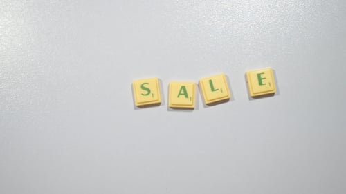 Hand Spells Out "Sale" with Letter Tiles