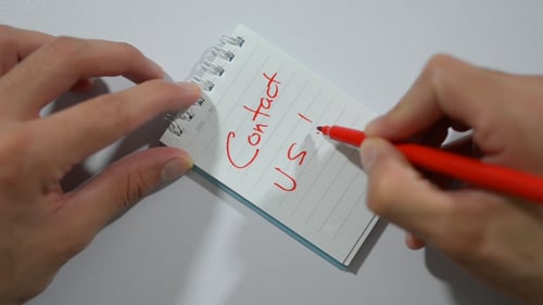 Writing 'Contact Us' on Spiral Notebook with Red Pen