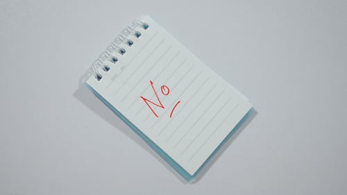 Hands Write 'No' on Lined Notepad with Red Pen