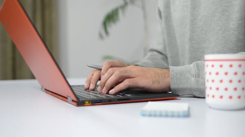 Person Typing on Laptop and Writing Notes