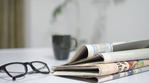 Newspaper Stacked Up Beside Mug and Glasses Indoors
