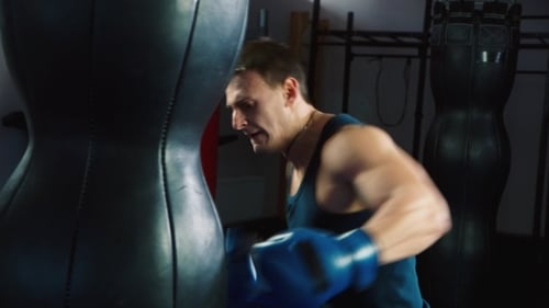 Muscular Man Punching Heavy Bag in Gym