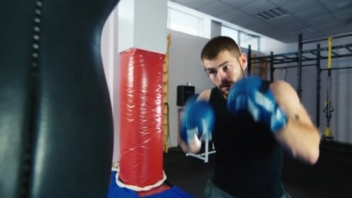 Athletic Young Man Punches Heavy Bag in Gym