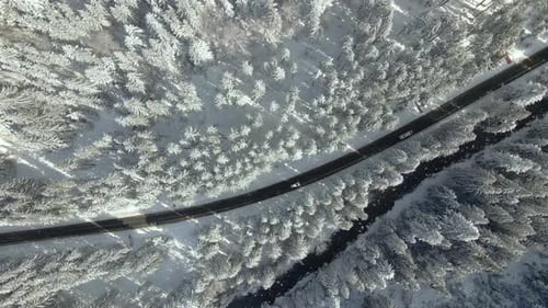 Aerial view of winter landscape with snow covered mountain hills and winding forest road in morning.