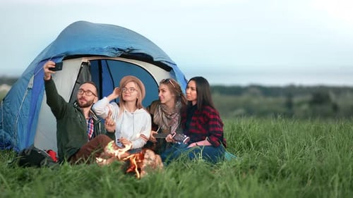 Casual Man and Woman Tourist Photographing Near Camp Tent and Campfire