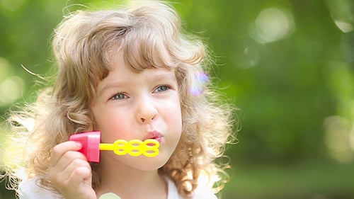 Child Blowing Bubbles in Sunny Green Setting