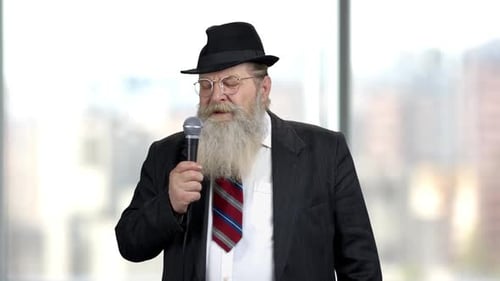 Mature Man Speaks into Microphone Wearing Suit and Hat