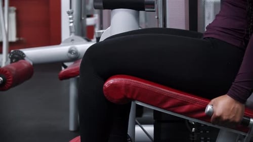 Uma mulher negra com tranças treinando as pernas em um equipamento de ginástica e mascando um chiclete