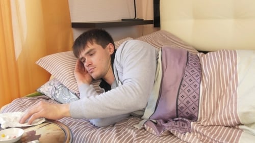 Man Blowing Nose While Sick in Bed