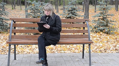 Woman Uses Tablet on Bench in Autumn Park