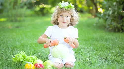 Child with Vegetables Playing on Green Lawn
