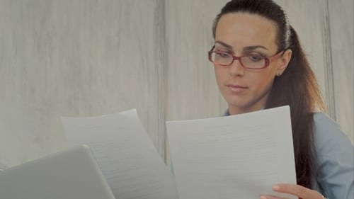 Woman Reviews Documents at Desk with Laptop