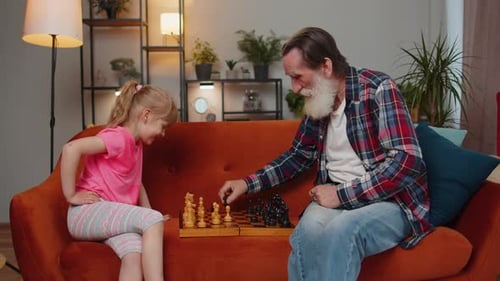 Smiling Senior Grandfather Playing Chess Board Game with Teen Granddaughter Child Girl Kid at Home