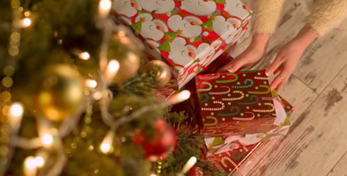 Woman Placing Christmas Presents Under Lit Christmas Tree